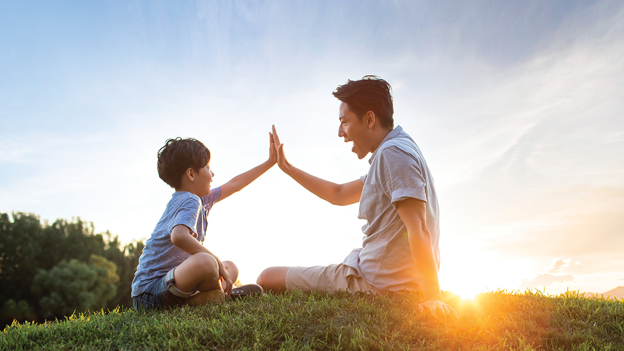 A father and son giving each other a high five on meadow.