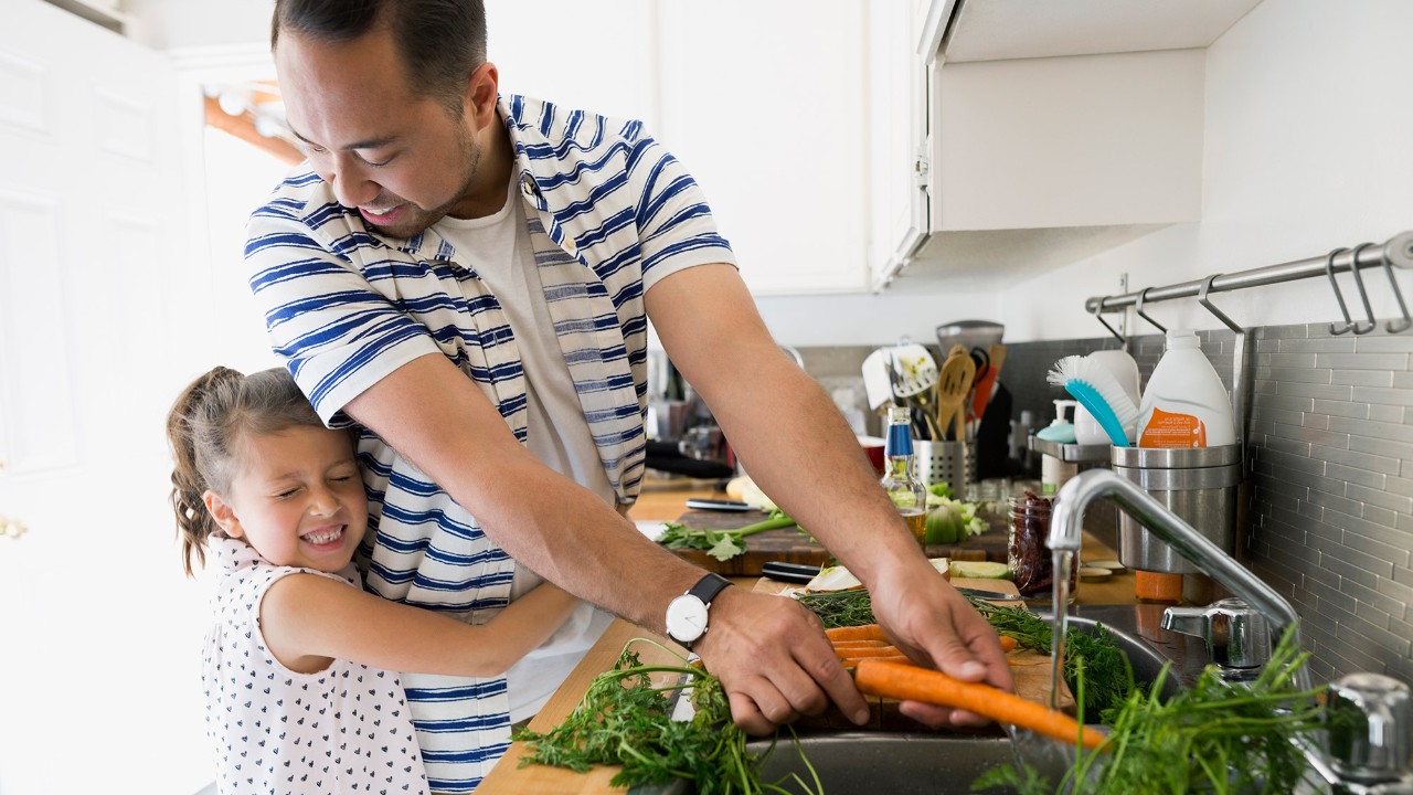 A father and daughter are washing vegetbales in kitchen; image used for HSBC Insurance products page.