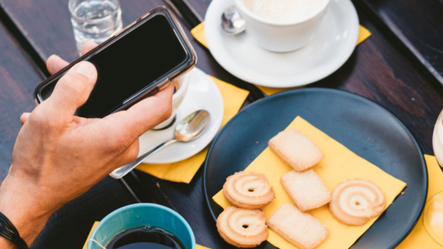 Person holding out mobile phone to take a picture of snacks; image used for HSBC Singapore Paynow article.