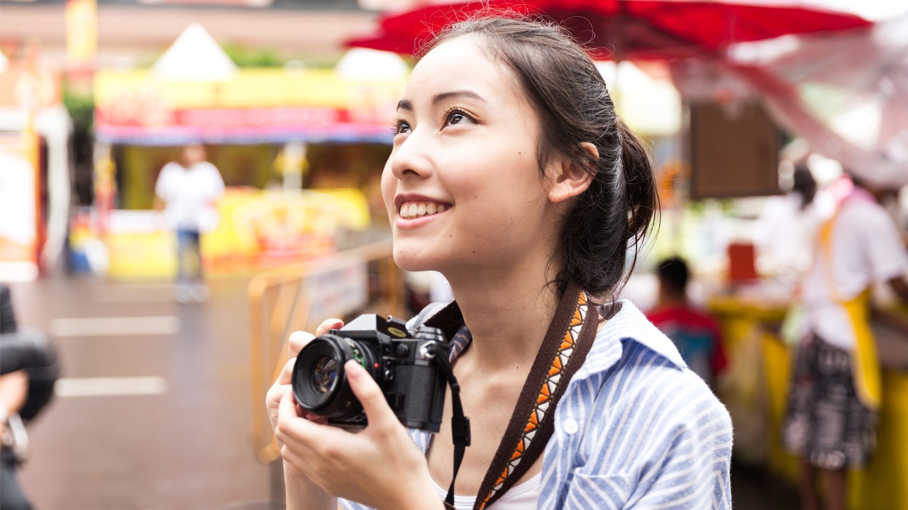 一位女士拿着相机；图片使用于汇丰新加坡多币种借记卡简介。