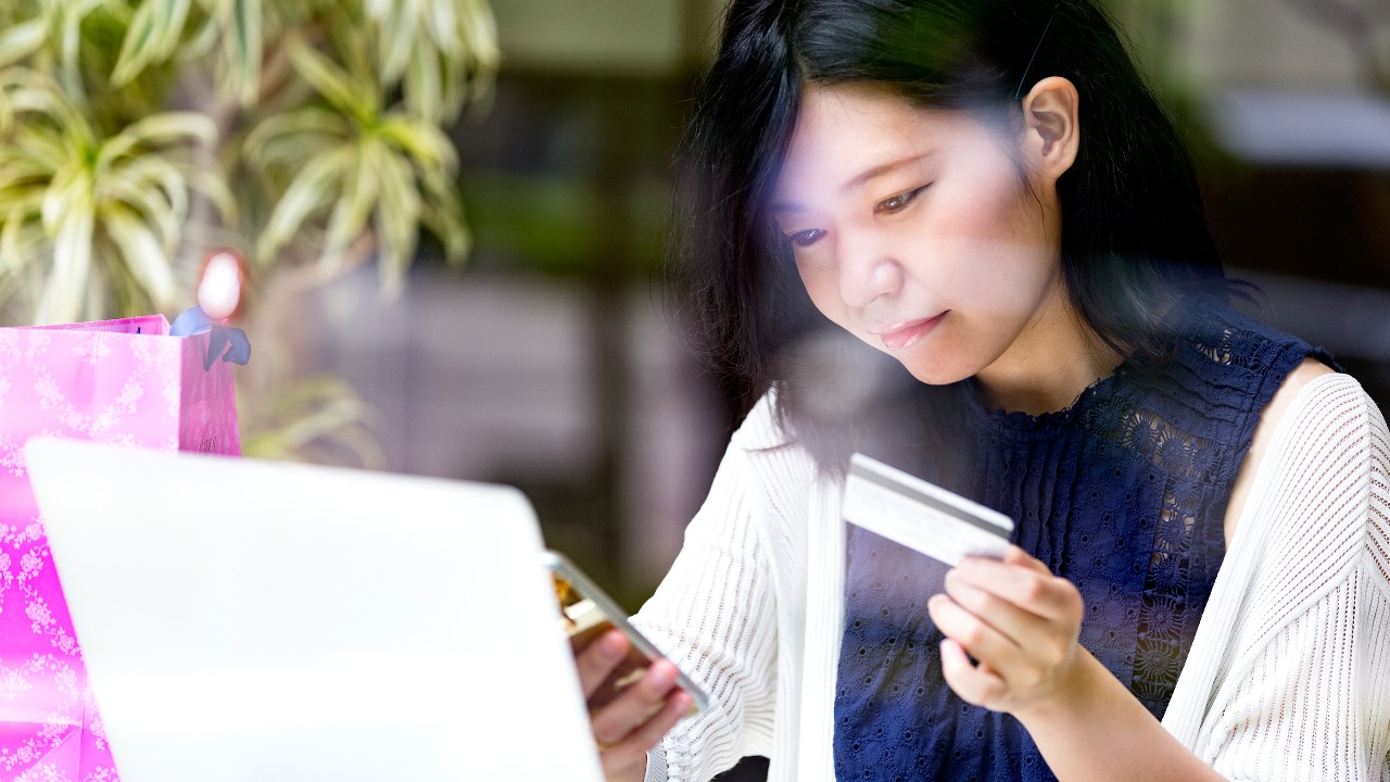 A woman holding a card while watching mobile phone.