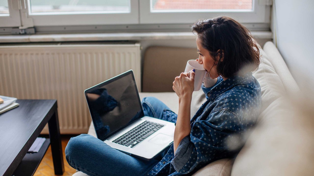 Woman using laptop and drinking.