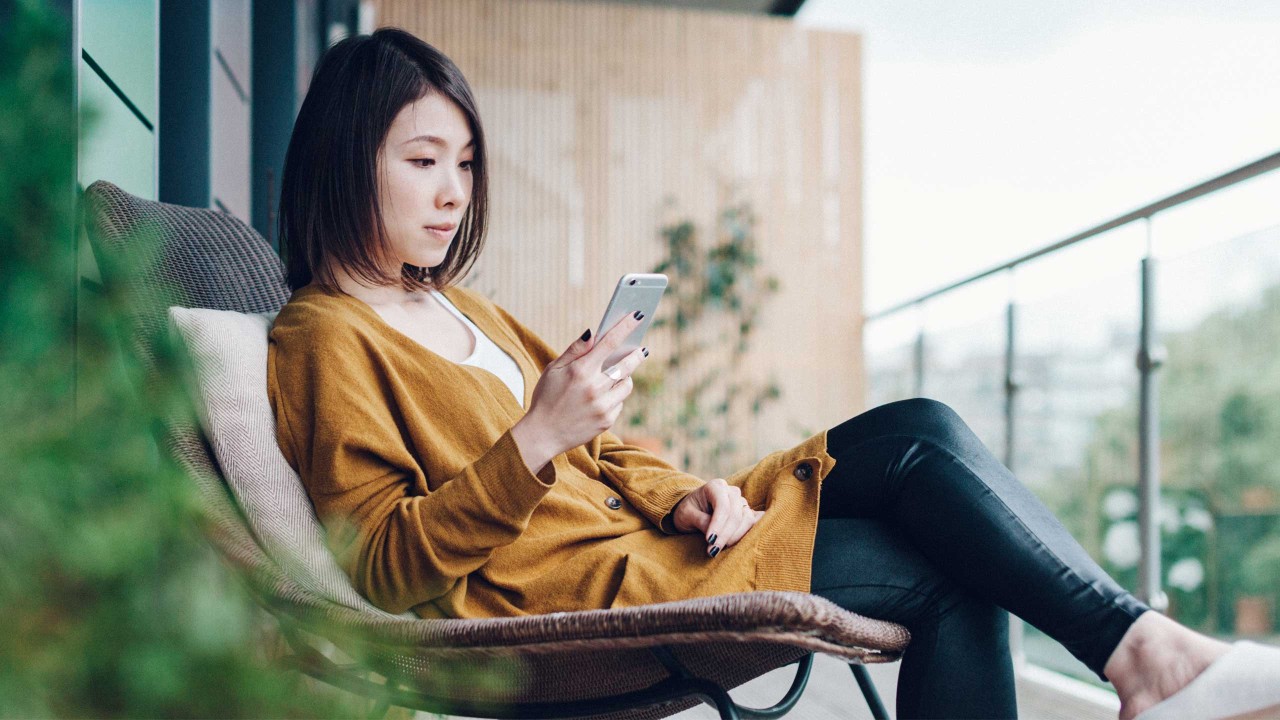 一位女子在阳台上使用智能手机；图片使用于汇丰新加坡多币种账户页面