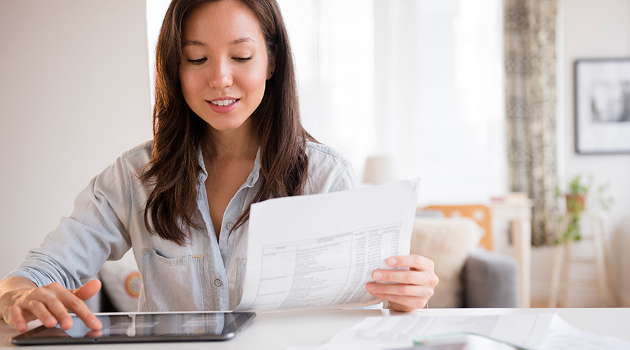 Woman holding statement and checking bank account on tablet; image used for HSBC Singapore Benefits of online banking article.