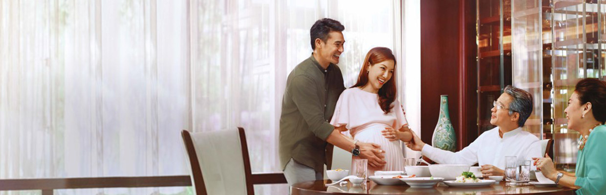 一个孕妇与丈夫和家人一起吃午餐，图片使用于汇丰翡翠传承万用寿险计划。