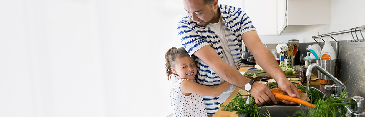 A father and daughter are washing vegetables in kitchen; image used for HSBC Insurance products page. 