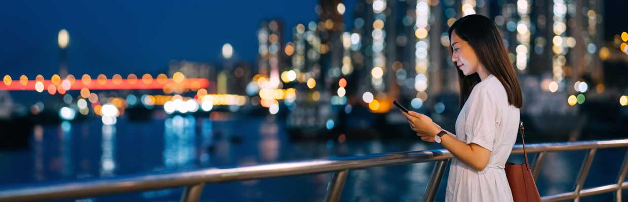 Young woman using smartphone by the promenade ; image used for HSBC Singapore All you need to know about ETFs article.