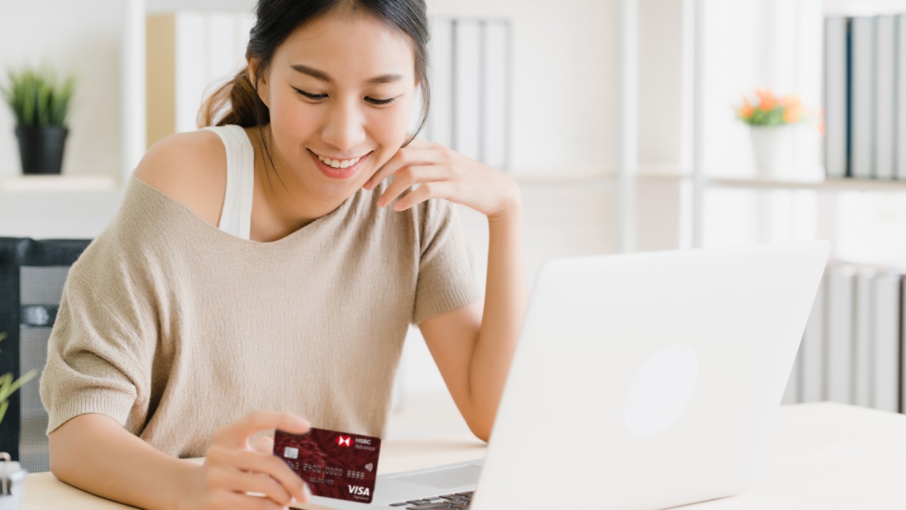 Woman using computer and holding credit card.
