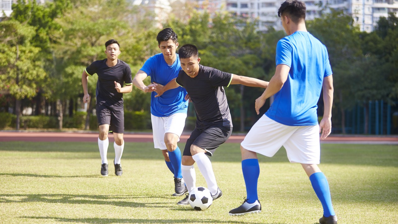年轻的亚洲成年男士正在踢足球。